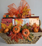 An autumn-themed fall gift basket filled with assorted packaged snacks and treats, decorated with orange and yellow artificial leaves, small pumpkins, and a large orange sheer bow.